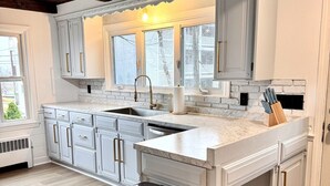 A modern kitchen with white cabinetry, a marble countertop, and a stainless steel trash can.
