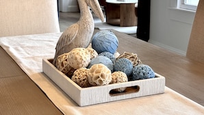 A wooden tray with decorative eggs on a textured fabric table in a room with a white door, a brown chair, and a window.