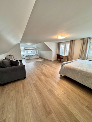 A bedroom with a bunk bed, a sofa, a desk, and a large window.