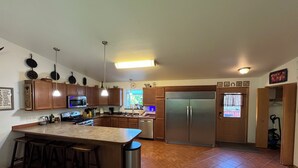 Una cocina moderna con armarios de madera, un refrigerador de acero inoxidable, una isla grande con taburetes y piso de baldosas.