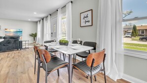 A dining area with a white table set for six, surrounded by black and wooden chairs.