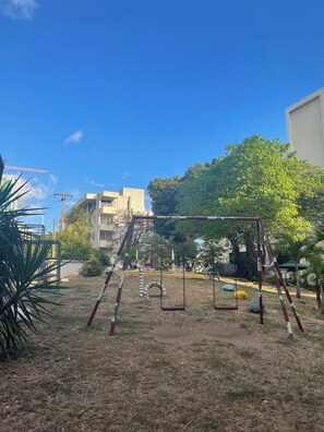 Un parque infantil con columpios y una estructura de escalada, rodeado de césped y árboles.