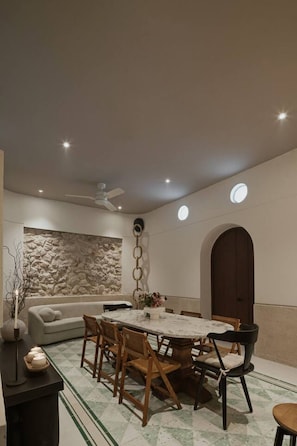 A dining area with a round table, wooden chairs, and a stone wall. - Casa Meraki Mérida - Paseo de Montejo (Centro)