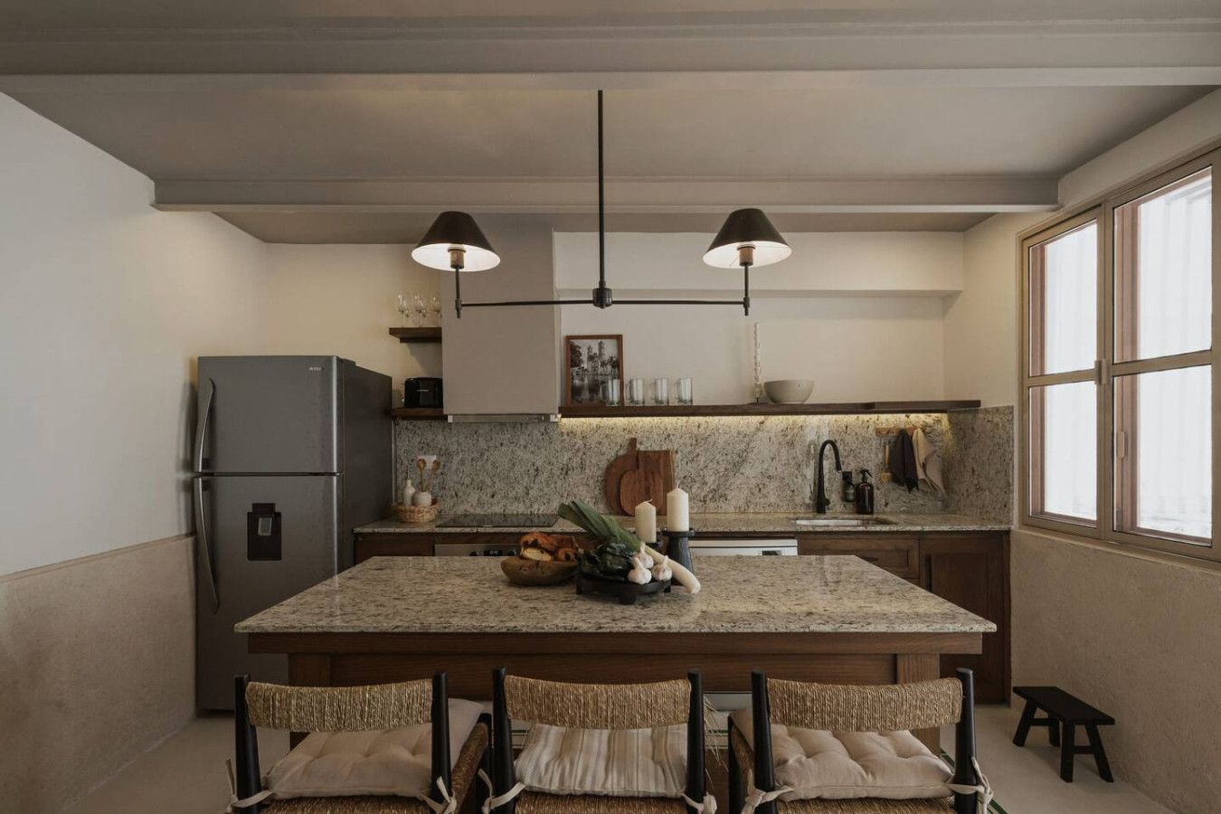 A modern kitchen with a central island, granite countertops, a stainless steel refrigerator, and pendant lighting.