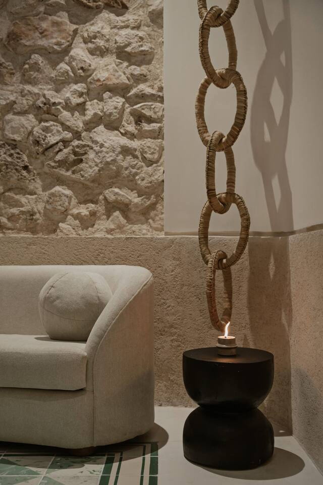 Un interior moderno con una pared de piedra texturizada, un sofá blanco con un cojín y una lámpara colgante original.
