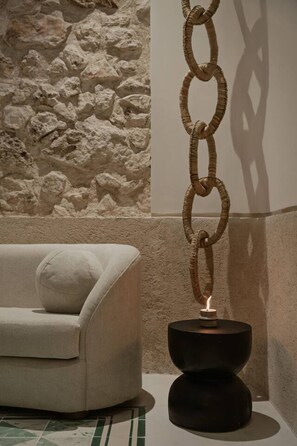 Un intérieur moderne avec un mur en pierre à texture, un canapé blanc agrémenté d’un coussin et un luminaire suspendu original.
