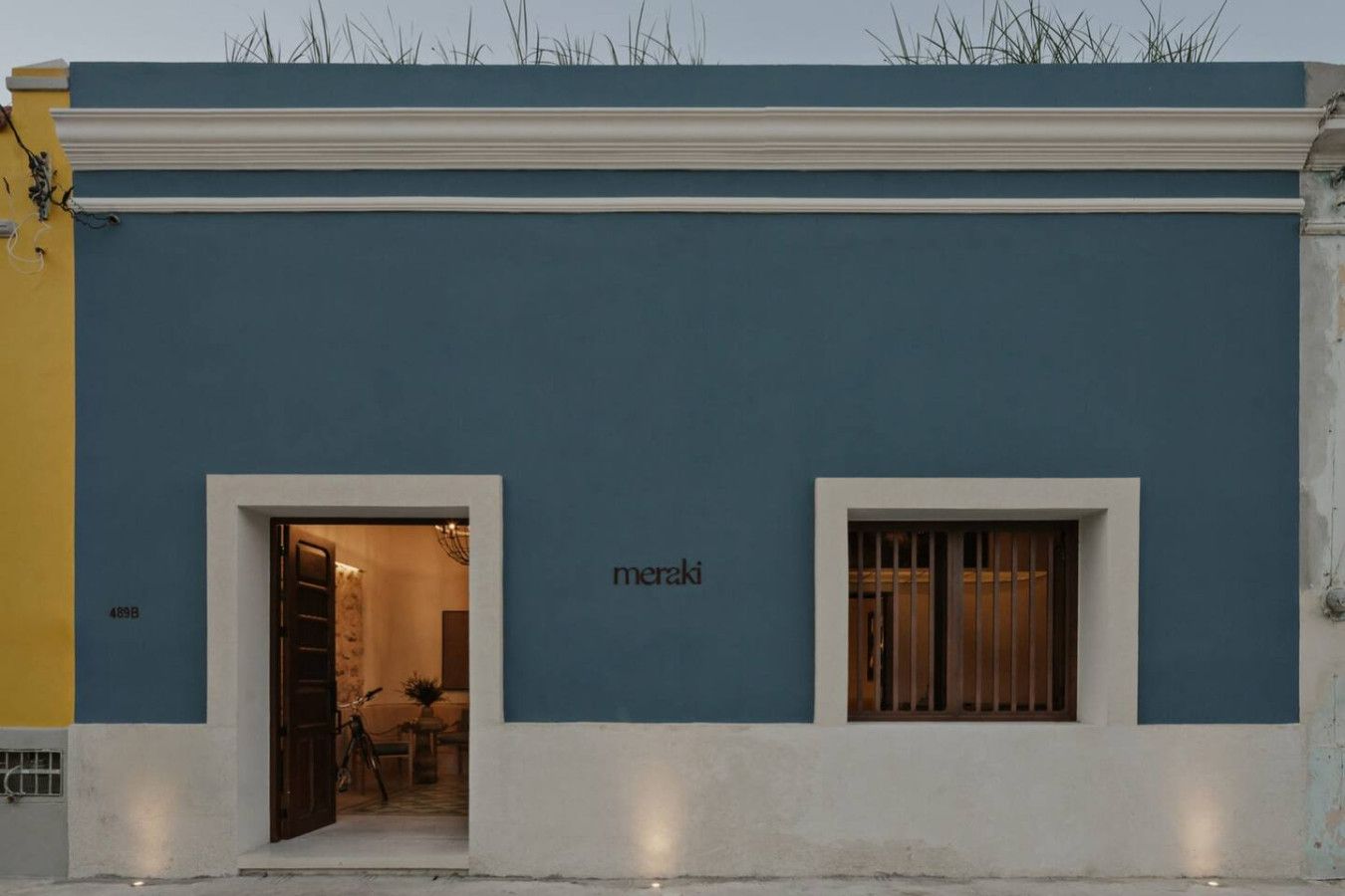A building with a blue facade, two small windows, and a door leading to an interior space.