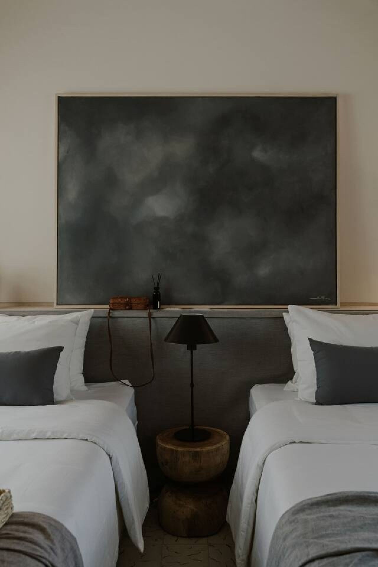 Habitación de hotel con dos camas, un cuadro abstracto grande en la pared, un taburete de madera pequeño y una lámpara de pie negra.