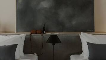 Habitación de hotel con dos camas, un cuadro abstracto grande en la pared, un taburete de madera pequeño y una lámpara de pie negra.