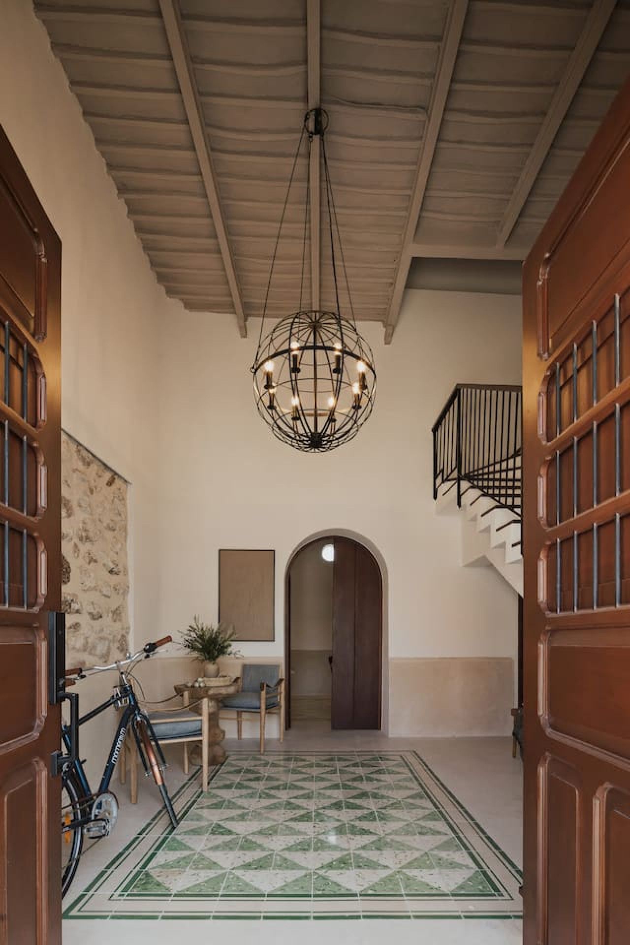A hallway with a geometric patterned floor, a bicycle, a table with chairs, and a chandelier.