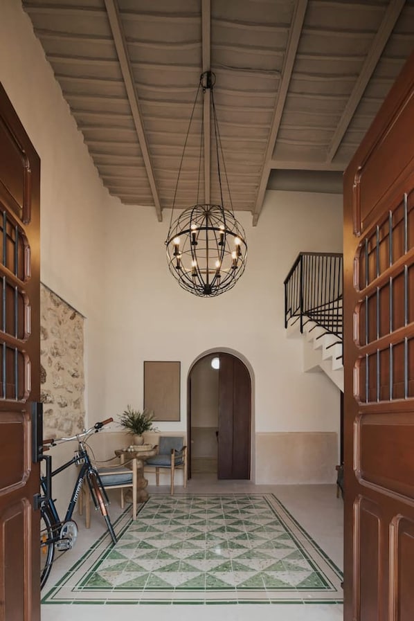 A hallway with a geometric patterned floor, a bicycle, a table with chairs, and a chandelier. - Casa Meraki Mérida - Paseo de Montejo (Centro)
