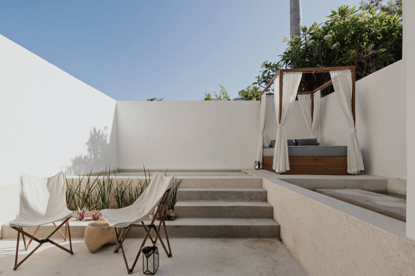 Un patio al aire libre minimalista con una cama de madera, un dosel y una mesa con sillas.