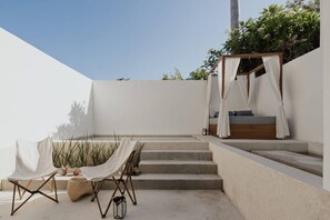 Terrassa exterior minimalista amb llit de fusta, una tenda i una taula amb cadires.