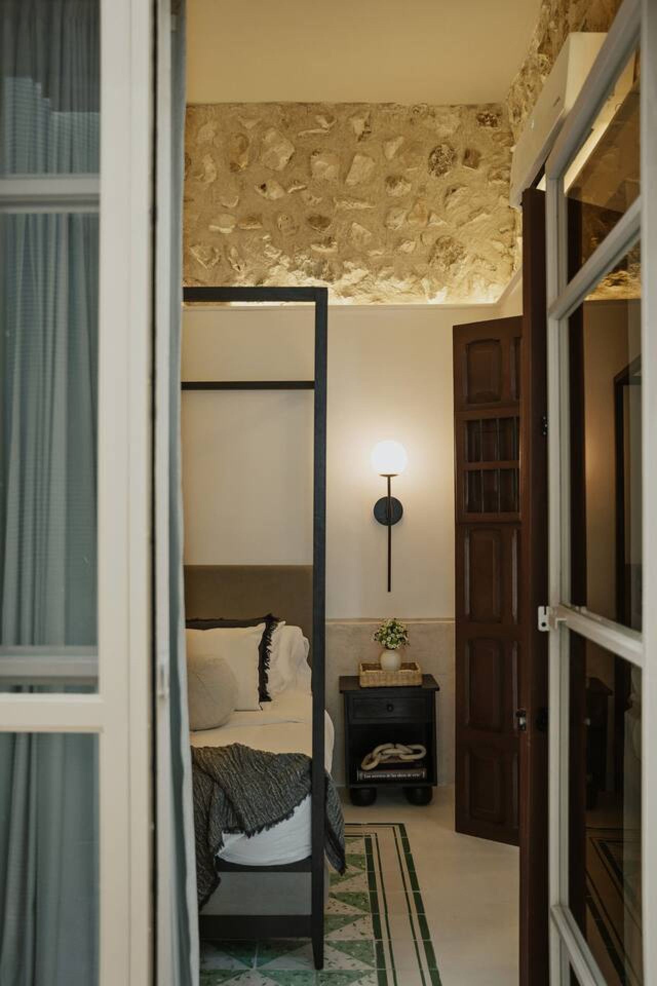 Un dormitorio con una cama, una mesita de noche, una lámpara de pared y una puerta.