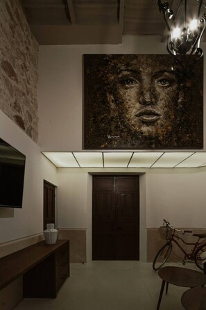 Un couloir orné d’un grand tableau abstrait, avec un banc en bois, une porte et un vélo.