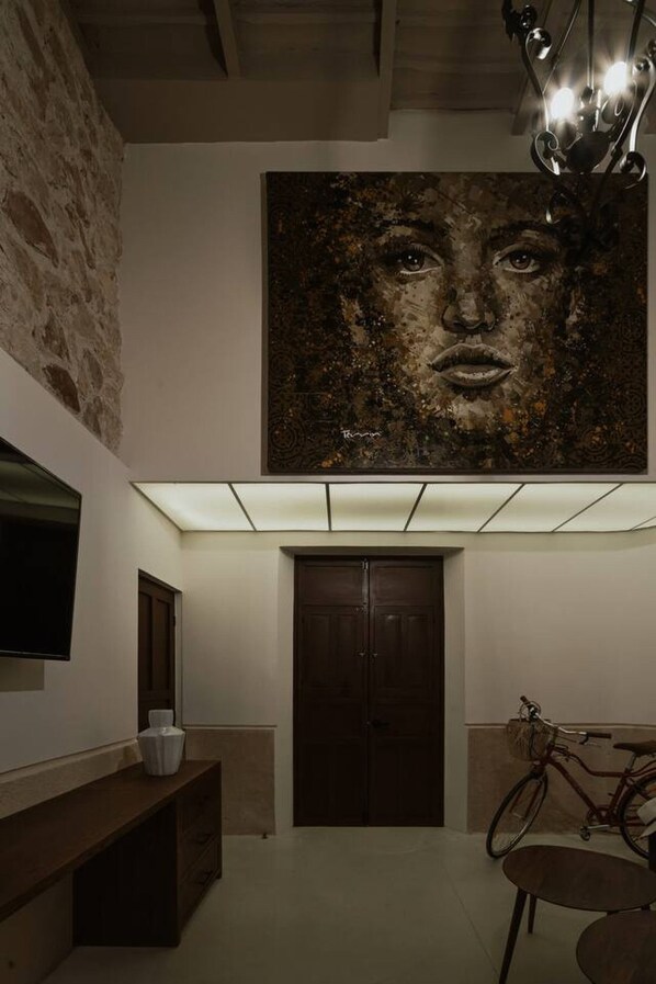 A hallway with a large abstract painting, a wooden bench, a door, and a bicycle. - Casa Meraki Mérida - Paseo de Montejo (Centro)