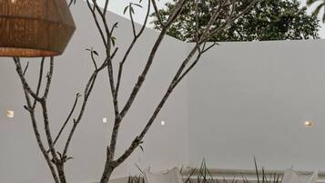 An outdoor seating area with a table and chairs, a hanging light fixture, and a tree with white flowers.
