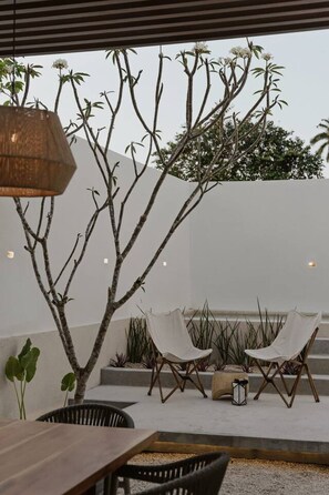 An outdoor seating area with a table and chairs, a hanging light fixture, and a tree with white flowers.