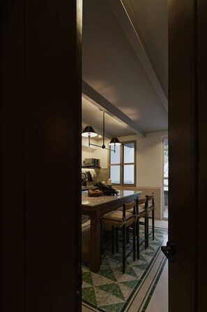Una cocina con un ventanal grande, una zona de comedor con sillas y piso de baldosas.