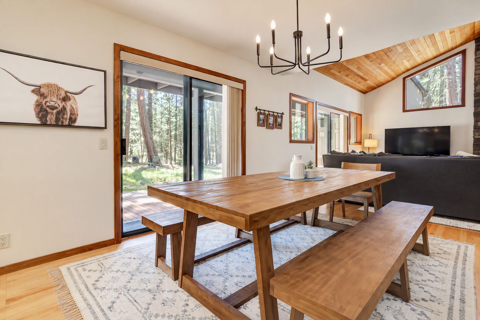 A modern interior with a wooden dining table, benches, a chandelier, and a large TV.