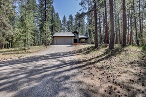 Une cabane à deux étages avec un garage, entourée d’une forêt.