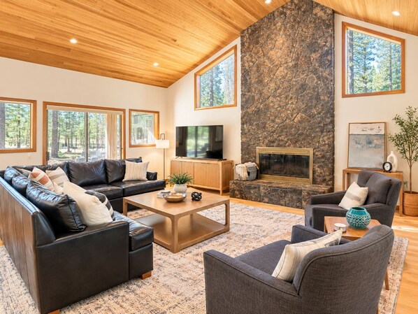 A spacious living room with a stone fireplace, leather sofas, and a television. - Secluded, Near Entrance w/ Hot Tub & Game Room! (Sisters)