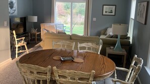 A dining area with a round wooden table and six chairs, a sofa, and a TV in the background. - Charming 2-bedroom condo with WiFi, AC in gorgeous Kitty Hawk (Kitty Hawk)