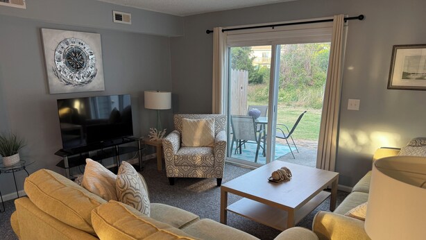 A living room with a sofa, a television, a lamp, a coffee table, and a chair. - Charming 2-bedroom condo with WiFi, AC in gorgeous Kitty Hawk (Kitty Hawk)