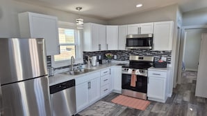 A modern kitchen with stainless steel appliances, white cabinetry, and a patterned backsplash. - Shadow Ridge Tiny Home (Big Cabin)