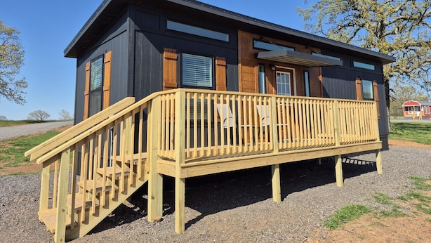 A modern building with a wooden deck, large windows, and a gravel ground. - Shadow Ridge Tiny Home (Big Cabin)