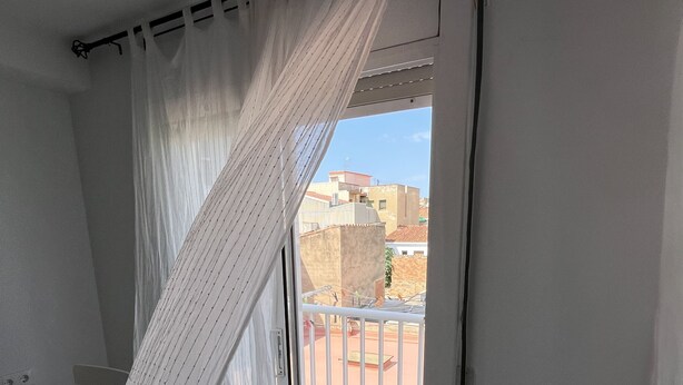 Un balcon avec un rideau blanc, une chaise et une vue sur les immeubles.