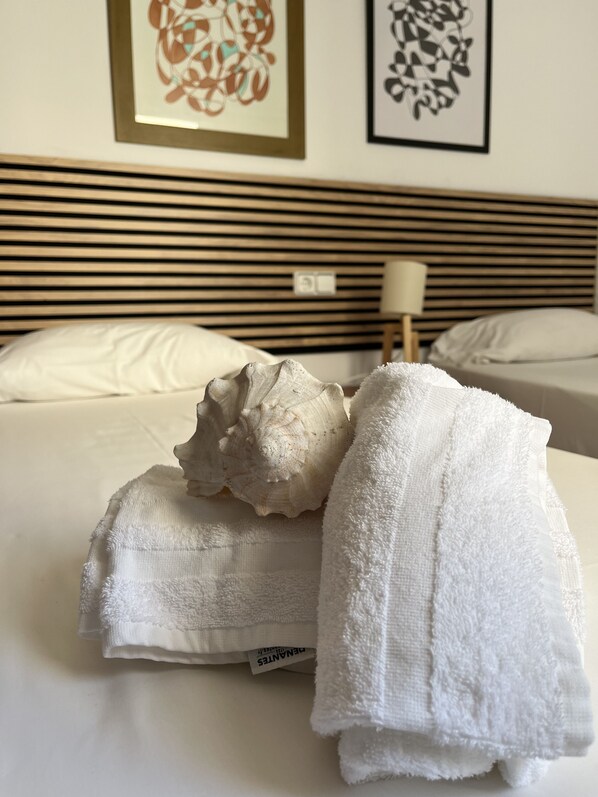 Una cama bien hecha con una concha marina grande y una toalla blanca doblada.