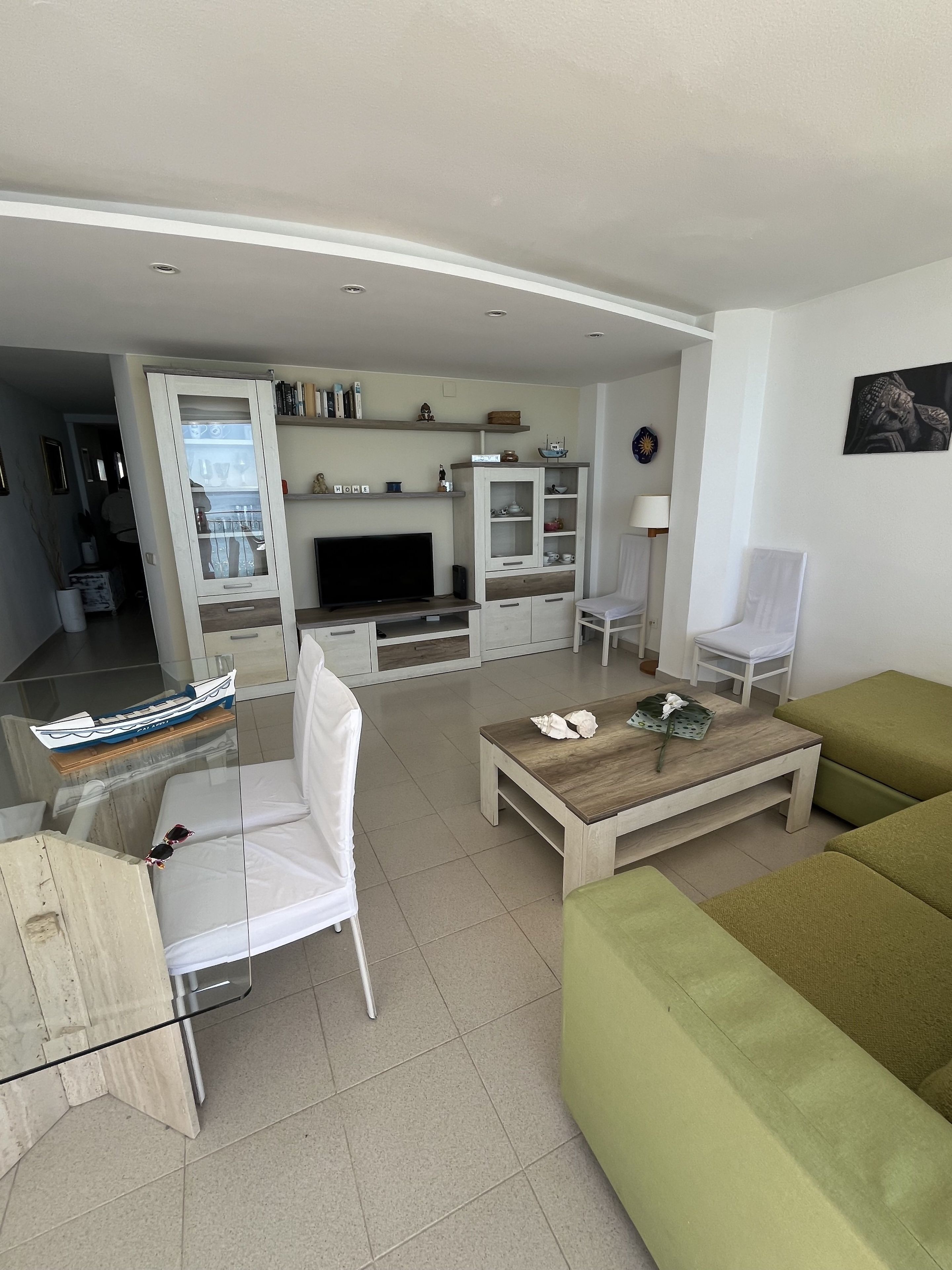 A modern living room with a sofa, a coffee table, a TV, and a cabinet with shelves.