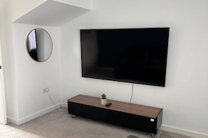 Uma sala de estar moderna com uma TV de tela plana na parede, um espelho redondo e um console de madeira com uma planta.