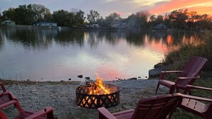 Eine Uferlandschaft mit Lagerfeuerstelle und roten Stühlen.