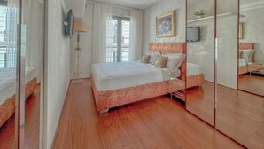 A bedroom with a bed, a mirror, a TV, and a window with curtains. - Luxury 2-Bedroom Apartment - Rue d'Antibes, Cannes (Cannes)