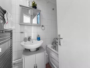 Ein modernes Badezimmer mit einem weißen Waschbecken, einem Spiegel darüber, einem Handtuchhalter und einer Badewanne.