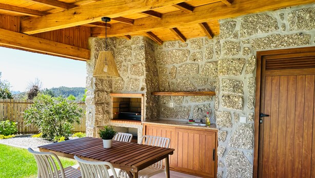 An outdoor kitchen area with a stone wall, wooden cabinets, and a table with chairs. - Casa do Sol e Vinho: Breathtaking views & oasis of peace villa (Ourilhe)