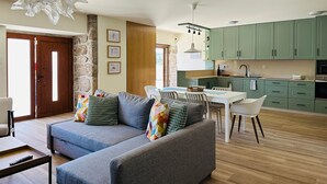 A living room with a grey sofa, a dining table with chairs, and a kitchen with green cabinets. - Casa do Sol e Vinho: Breathtaking views & oasis of peace villa (Ourilhe)