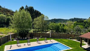 A rectangular swimming pool with a wooden deck, surrounded by a wooden fence and a grassy lawn. - Casa do Sol e Vinho: Breathtaking views & oasis of peace villa (Ourilhe)