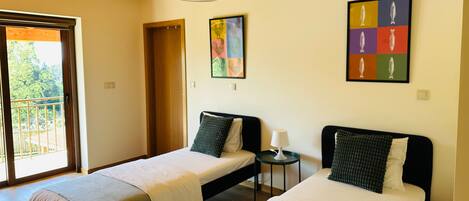 A room with two beds, a small table, and a door leading to a balcony.