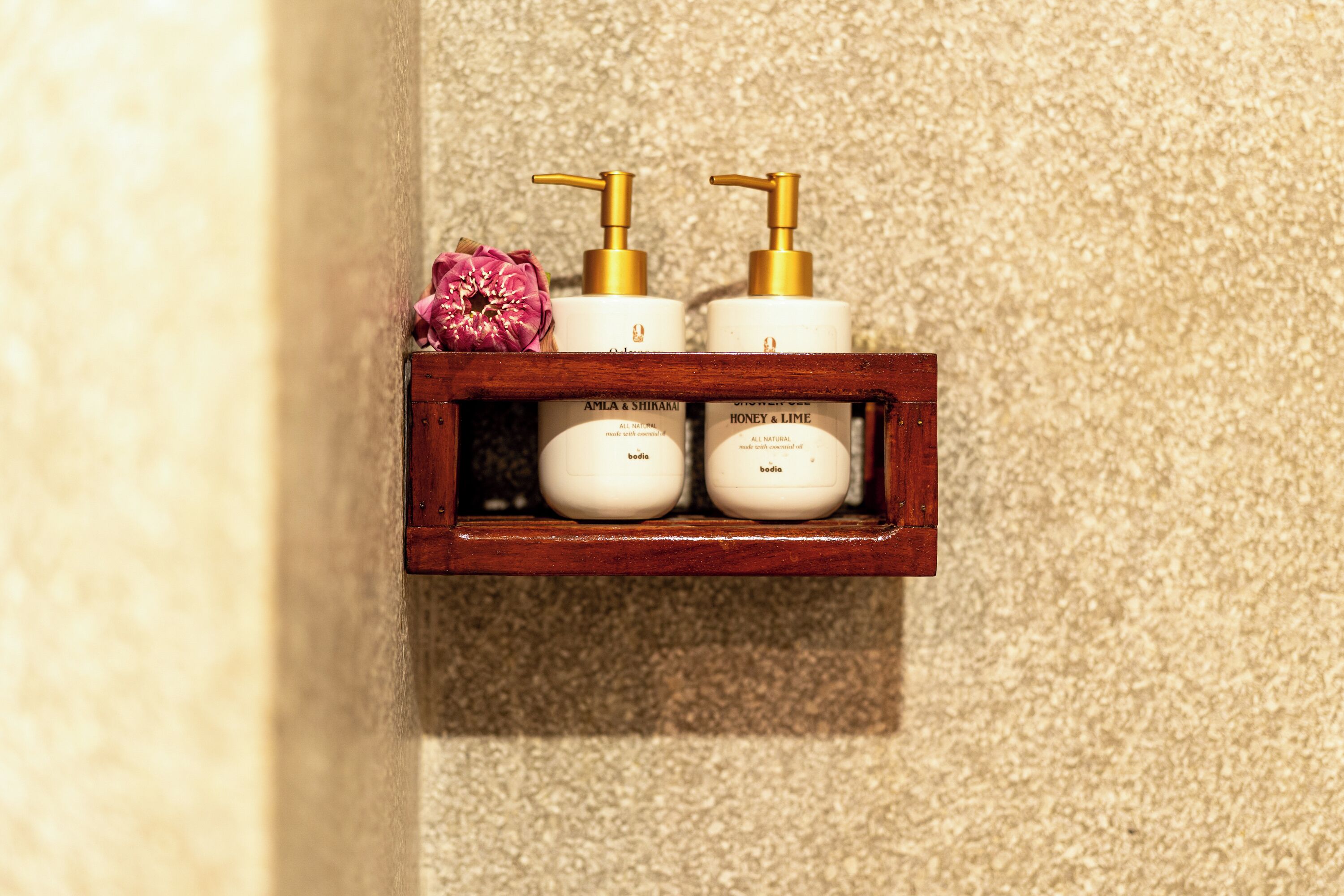 Una estantería de madera con tres productos para el cuidado de la piel y una flor rosa.