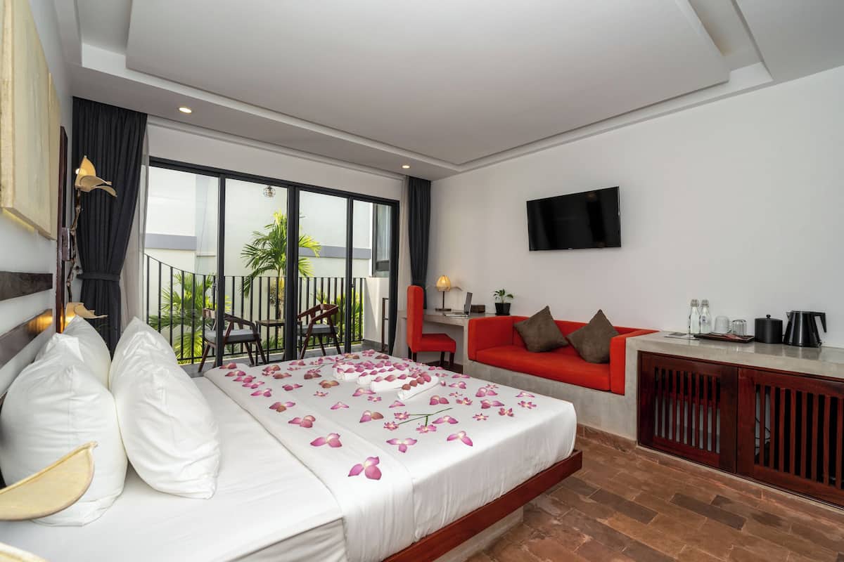 Une chambre d’hôtel avec un lit, un canapé rouge, une télévision et un balcon donnant sur un paysage verdoyant.