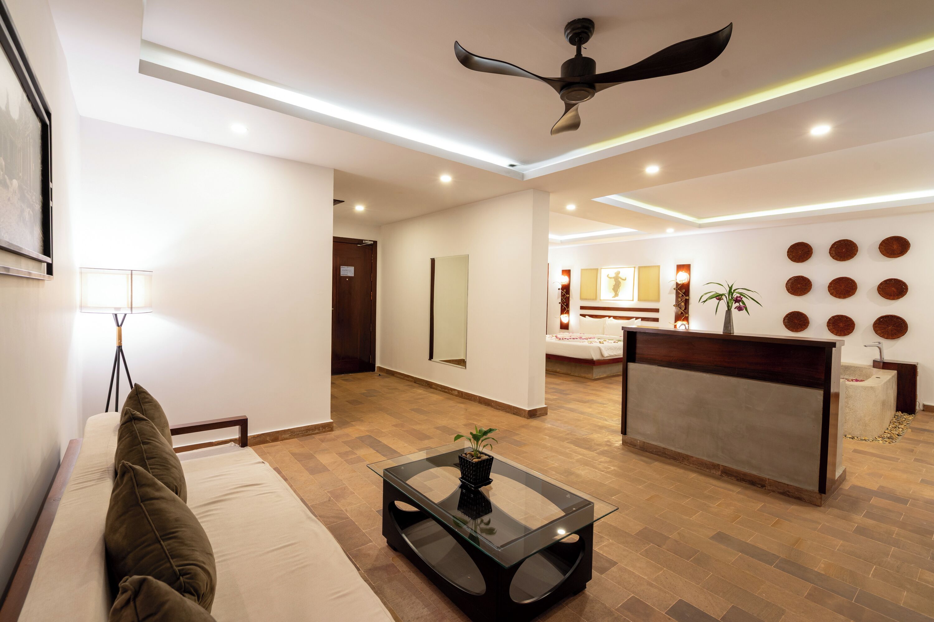 A modern living room with a glass coffee table, a sofa, a ceiling fan, and a reception desk.