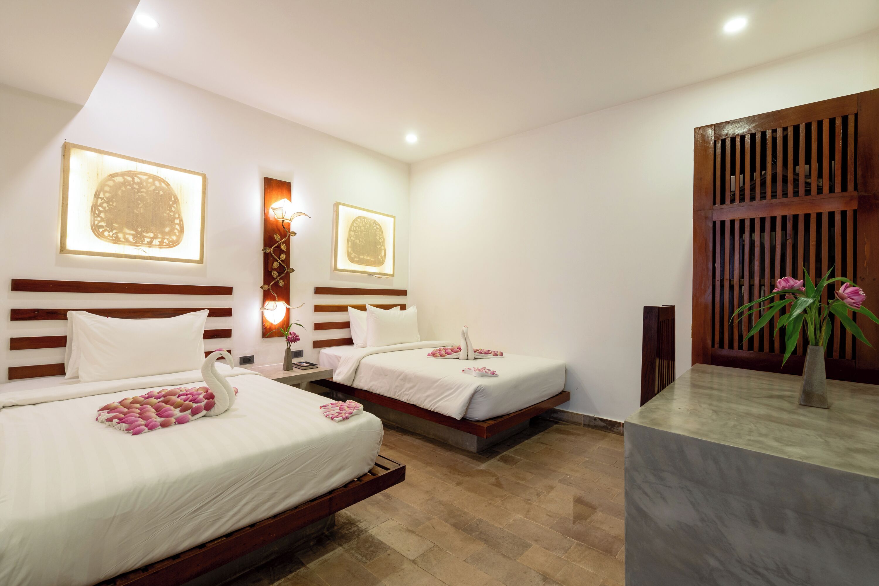 A hotel room with two beds, a wooden headboard, a marble reception desk, and a wall-mounted light fixture.