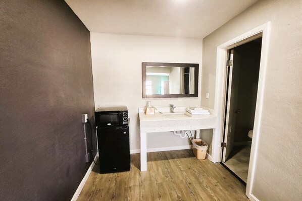 Une salle de bain avec un lavabo blanc, un miroir et un appareil noir, qui pourrait être un lave-linge ou un sèche-linge.