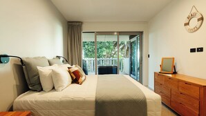 Un dormitorio con cama, mesita de noche, cómoda y vistas a un balcón con valla blanca.