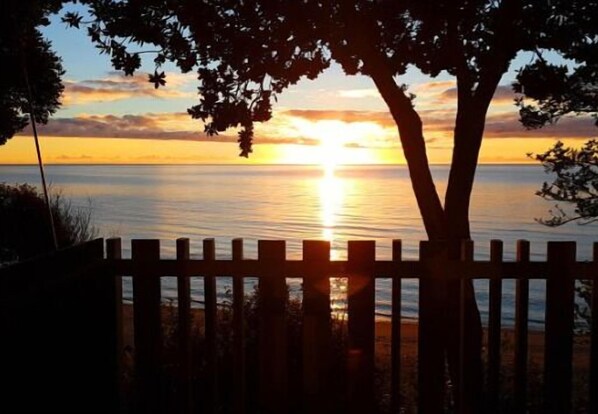 A sunset over a calm body of water, viewed through a wooden fence.