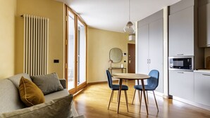 Un salon moderne comprenant un canapé, une table à manger avec des chaises, un coin cuisine avec des placards et des appareils électroménagers, et une grande fenêtre.