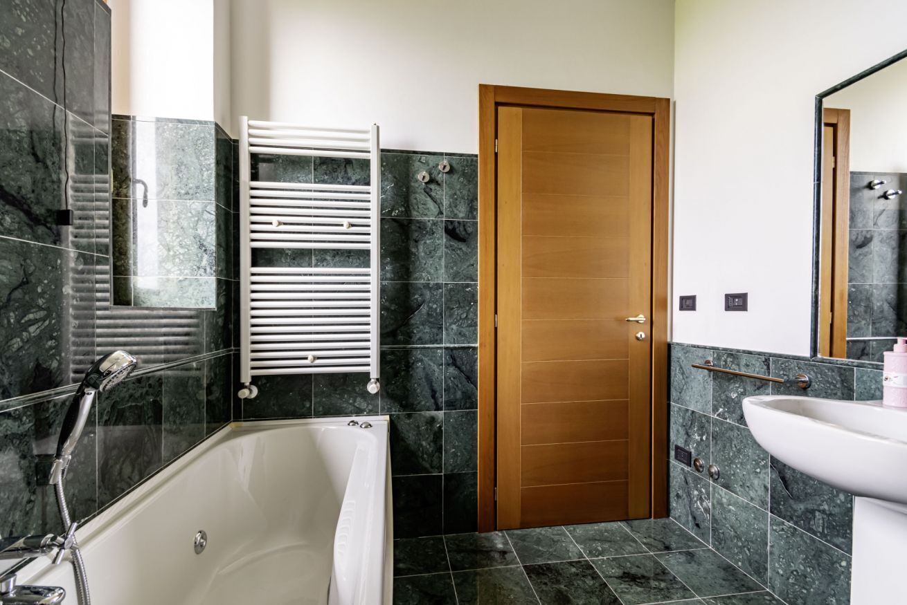 A bathroom with a bathtub, a wooden door, a towel rack, and a sink.